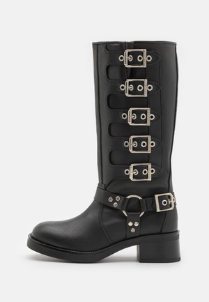 Botte en cuir noire mi-mollet avec cinq sangles à boucles argentées sur le côté et un petit talon épais.