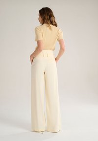 Haut à manches courtes côtelé beige clair associé à un pantalon large taille haute crème, présentant une texture lisse et des détails subtils sur la ceinture.