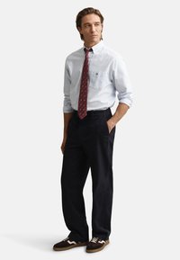 Šviesiai mėlyna su dryželiais mygtukais užsegama marškiniai, tamsios kelnės ir rudi sportbačiai su baltais akcentais. Yra raudonas raštuotas kaklaraištis ir krūtinės kišenė.