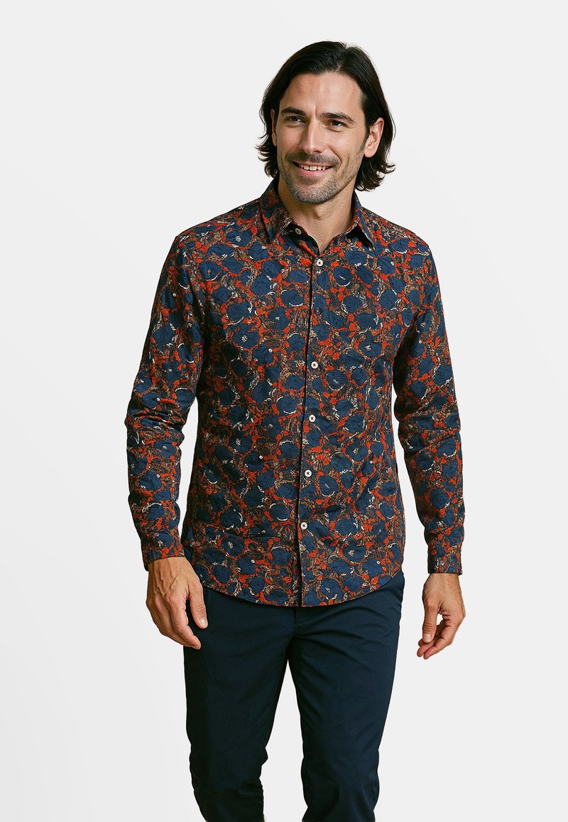 Donkerblauwe blouse met een bloemenpatroon in rood en wit. Lange mouwen en een puntige kraag. Gemaakt van een zachte stof.