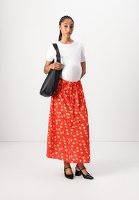 Rode bloemenmaxi-rok met een koord in de taille, gecombineerd met een wit T-shirt. Een zwarte schoudertas en zwarte hakken maken de look compleet.