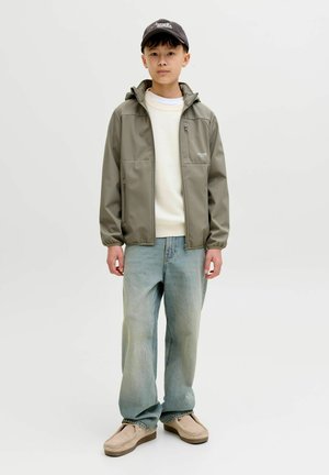 Veste vert olive résistante à l'eau avec capuche, deux poches avant, associée à un pull crème, un jean ample bleu clair et des chaussures beige à enfiler.