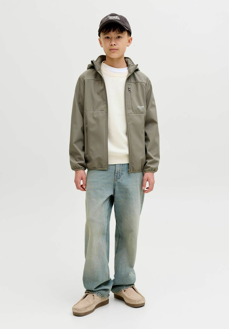 Vodootporna maslinasto zelena jakna s kapuljačom, dva prednja džepa, u kombinaciji s krem džemperom, svijetloplavim širokim trapericama i bež cipelicama bez vezica.