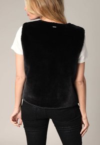Zwart, faux fur vest met een hoge kraag en mouwloos ontwerp, gecombineerd met een wit T-shirt en zwart gemeleerde broek. Gladde textuur.