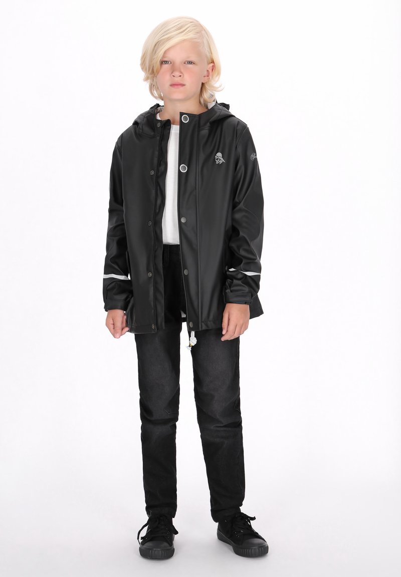 Melnā ūdensnecaurlaidīgā jaka ar kapuci, spiedpogu aizdari un baltām akcentiem. Valkāta virs baltas krekla un kombinēta ar melniem biksēm un apaviem.