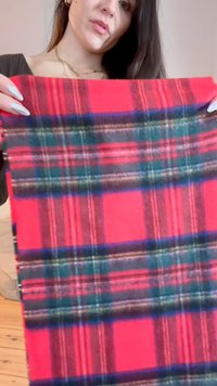 Rød plaid stof med grønne og blå nuancer. Materialet ser blødt ud med en vævet tekstur, der viser klare horisontale og vertikale linjer.