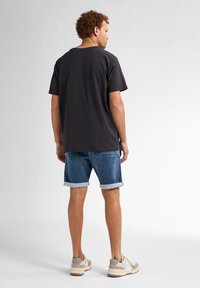 Černé bavlněné tričko s kulatým výstřihem, doplněné o modré džíny s ohrnutými manžetami. Outfit doplňují tenisky v neutrálních tónech.