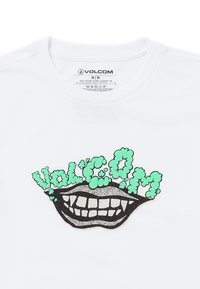Camiseta de algodón blanca con un gráfico negro y brillante de una boca sonriente, con el texto verde "Volc.Om" arriba, en una fuente divertida.