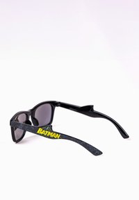 Black sunglasses with dark lenses and Batman-themed accents on the arms. Text "BATMAN" in yellow on the left arm, textured black finish.