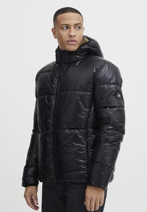 Svart puffjacka med glänsande yta, utrustad med horisontell söm, dragkedja och huva. Accentlogotyp på ärmen.