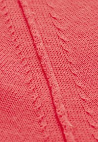 Korallenfarbener Strickstoff mit erhöhten Kabelmustern und glatter Textur, mit einer vertikalen Naht, die in der Mitte verläuft.