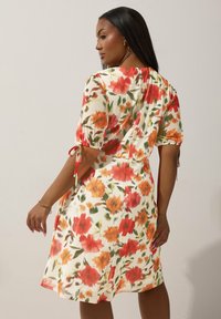 Kwiatowa sukienka z pomarańczowymi i czerwonymi kwiatami na kremowym tle, krótki rękaw z wiązaniami oraz luźny krój.