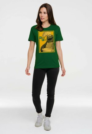 Frau trägt ein grünes T-Shirt mit einer Cartoon-Figur mit Kochmütze, die eine Schüssel hält mit dem Text "Baking Bread" auf gelbem Hintergrund.
