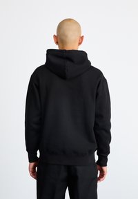 Μαύρη κουκούλα φτιαγμένη από μαλακό ύφασμα, με ευρύχωρη κουκούλα, ριμπ μανσέτες και στρίφωμα; λεία υφή με καθαρό, μινιμαλιστικό σχέδιο.