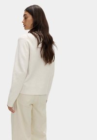 Světle béžový svetr s ribovaným spodním lemem a manžetami, vyrobený z měkké tkaniny, má jednoduchý design a volný střih. Nenošené světle zbarvené kalhoty.