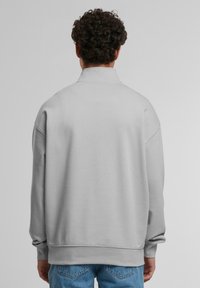 Grey sweatshirt with a high collar, oversized fit, and ribbed cuffs. Made of a soft material with a smooth texture.