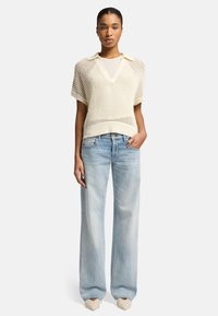 Maglione a maglia crema a maniche corte con scollo a V e colletto, abbinato a jeans azzurri a gamba larga e scarpe beige a punta.