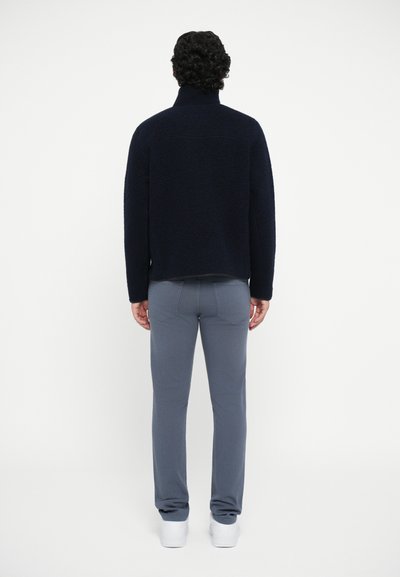 Marineblaue Fleece-Jacke mit Reißverschluss und hohem Kragen, kombiniert mit hellgrauen Slim-Fit-Hosen und weißen Sneakern. Rückansicht, minimalistische Details.