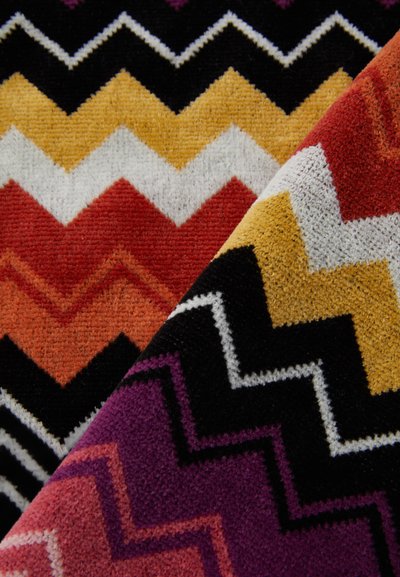 Multicolored zigzag patterned fabric featuring red, orange, yellow, black, and white hues with a textured, fuzzy surface.