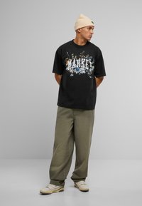 Sort grafisk t-shirt med farverig print med ordet "MARKER", parret med olivenfarvede vide bukser og cremede sneakers.