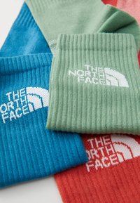 Fargerike strikkede sokker i blått, grønt og rødt, med ribbestruktur og "The North Face"-logo i hvitt på hver sokk.
