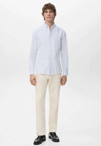 Camisa azul clara a rayas con cuello, cierre de botones, mangas largas; combinada con pantalones color crema y zapatos negros. Diseño minimalista.