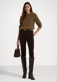 Καφέ πουλόβερ με πλέξη κάλτσας, καφέ κομμένα παντελόνια, καφέ μπότες μέχρι το γόνατο με φερμουάρ και μια μικρή καφέ τσάντα. Απλές χρυσές λεπτομέρειες.