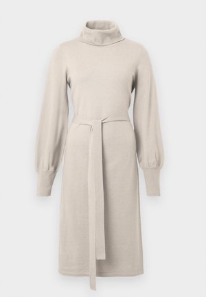 Bežinė megzta suknelė su aukštu apykakle, ilgomis pūkuotomis rankovėmis ir juosta juosmens srityje. Suknelė turi tiesų siluetą su briaunotais akcentais.