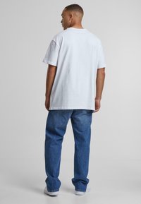 Camiseta blanca de algodón con cuello redondo, mangas cortas y un corte relajado, combinada con jeans de mezclilla azules que presentan costuras visibles y bolsillos.
