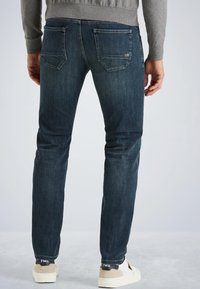Donkerblauwe denim jeans met een slim fit, voorzien van achterzakken en subtiele stikdetails, gecombineerd met witte sneakers.