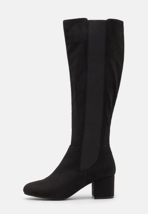 Botte haute en daim noir avec talon bloc et large panneau élastique sur le côté, conçue pour faciliter le port et le confort.