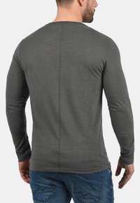 Grå langærmet T-shirt med rund hals og detalje med søm bagpå, lavet af et blødt, tekstureret stof. Bæres med blå jeans.