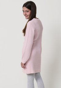 Abito maglione rosa a maglia con maniche lunghe, colletto rotondo e tessuto testurizzato; indossato sopra leggings grigi chiari.