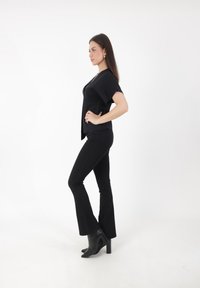 Schwarzes, enganliegendes Oberteil mit kurzen Ärmeln, kombiniert mit schwarzen, weit geschnittenen Jeans. Das Outfit wird durch spitze schwarze Ankle-Boots mit einem Blockabsatz ergänzt.