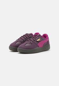 Chaussures de sport violettes avec semelles en caoutchouc gris foncé, accents roses, tissu texturé et un design classique à lacets. Présente un logo doré.