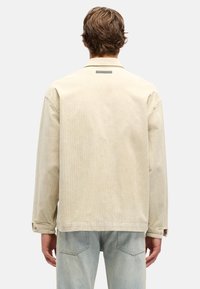 Beżowa kurtka koszulowa z sztruksu z długimi rękawami, kołnierzem z klapami oraz mankietami na guziki, z delikatnym, fakturowanym wzorem na tkaninie.