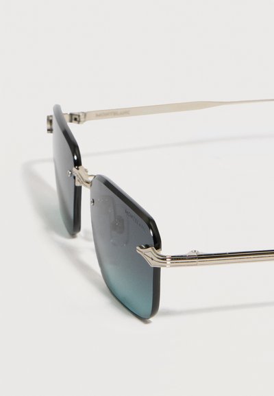 Ορθογώνια γυαλιά ηλίου με μαύρο σκελετό, φακούς με βαθμιαία σκουρότητα και λεπτά χρυσά μπράτσα, τοποθετημένα σε λευκή επιφάνεια.