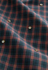 Un tissu à carreaux bleu, vert et bordeaux orné de clous dorés avec des embellissements transparents dispersés sur la surface.