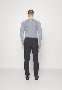 Pitkähihainen, vaaleanharmaa urheilupaita, jossa on teksturoitu kuvio, ja tummanharmaat vaellushousut, molemmat yhdistetty mustiin kenkiin. Takaviistosta kuvattuna.