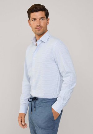 Hellblau karierter Hemd mit klassischem Kragen, kombiniert mit dunkelblauen Hose mit Kordelzug, was einen entspannten, maßgeschneiderten Look unterstreicht.