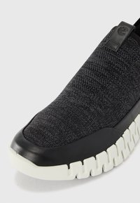 Black knitted slip-on shoe with a textured upper, a black rubber toe cap, and a chunky white outsole featuring zigzag patterns.