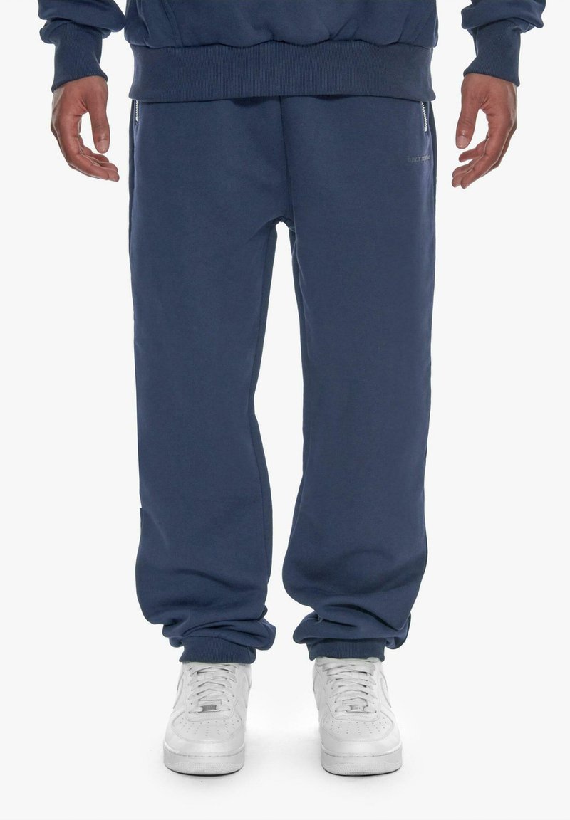 Marineblaue Sweatpants aus weichem Material, mit einem elastischen Bund und Bündchen, sowie seitlichen Reißverschlusstaschen zur Aufbewahrung.