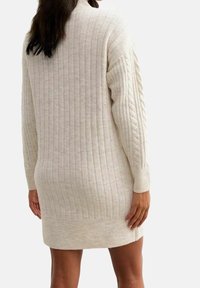 Robe en tricot beige clair avec une texture en côtes verticales, manches longues et accents en tricot torsadé sur les bras.