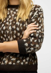 Brown and cream patterned knit sweater with a round neckline and ribbed cuffs. The fabric has a soft texture and a loose fit.