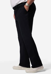 Mörkblå byxor i en bomullsblandning med rak bendesign, med sidofickor och matchade med ljusa sportskor.