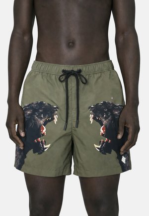 Costume da bagno verde con coulisse nera, con stampe di pantere nere ruggenti su ogni gamba, indossato da una persona di carnagione scura dalla vita alla metà coscia.