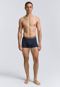 Tumši zili bokseršorti ar zaļu elastīgu jostasvietu, izgatavoti no gludas materiāla, pieguļošā dizainā un vidēja auguma garumā līdz augšstilbiem.