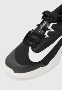Nike skriešanas apavi ar melnu sietu augšdaļu, baltu swoosh logotipu, teksturētu gumijas zoli un tradicionālu atkāpinājumu sistēmu.