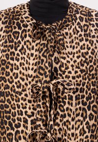 Μπλούζα με λεοπάρ σχέδιο και φ gathered λαιμόκοψη, διαθέτει μαύρες ταινίες και μαλακό, υφασμάτινο ύφασμα, με μοτίβο σε διάφορους τόνους καφέ και μαύρου.