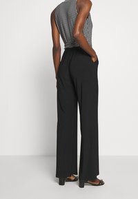 Svarta vida byxor med hög midja och fickor, i kombination med en mönstrad linne med rutmönster i svart och vitt.